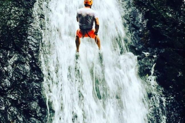 Person in helmet rappelling down a waterfall.