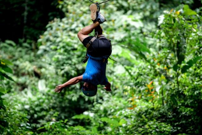 Person upside down ziplining through lush green forest.