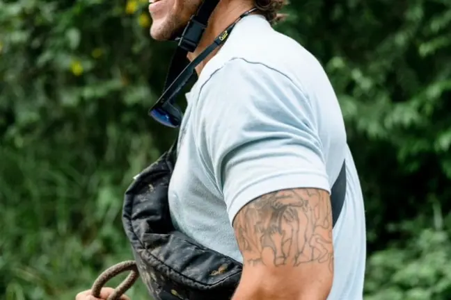 Man in blue helmet riding a horse, smiling with greenery in background.