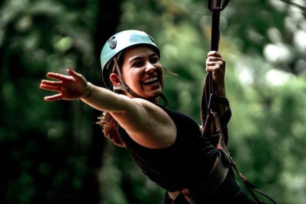 Smiling woman wearing helmet zip-lining through a forest.