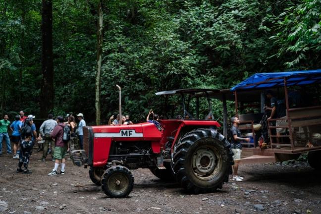 Group of people near a red tractor in a forest setting.