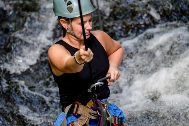 Woman with helmet and harness rappelling down a waterfall.