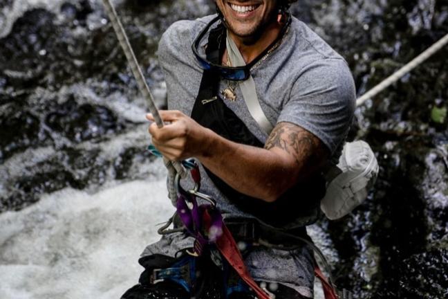 Smiling person rappelling down a waterfall wearing a helmet and harness.
