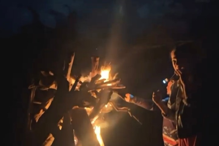 People around a campfire at night, one holding a flashlight.