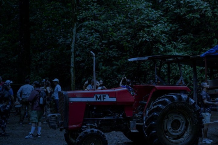 Red tractor in forest with people standing nearby, under dim light.