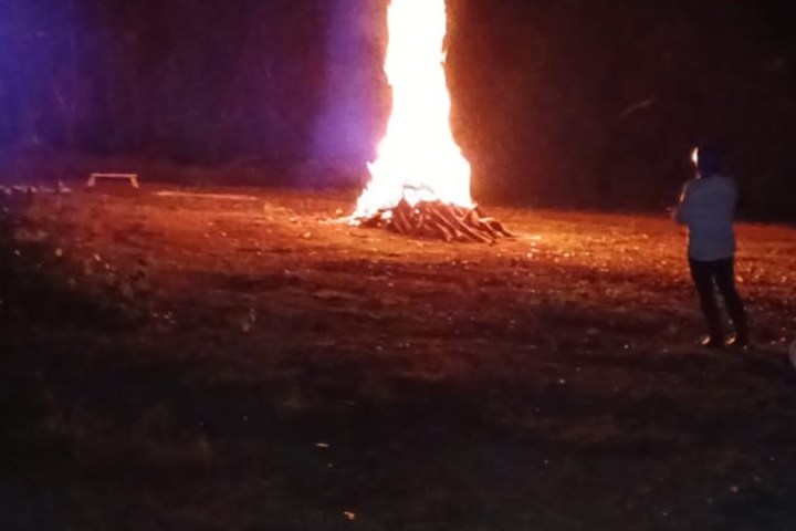 Large bonfire burning at night with a person standing nearby.