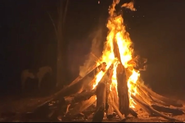 Large bonfire burning brightly in a dark outdoor setting at night.