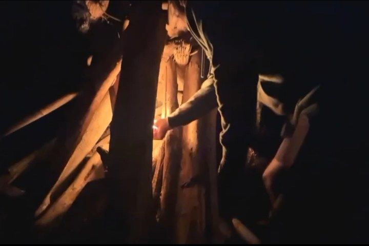 Person lighting a campfire at night with large logs arranged in a teepee shape.
